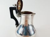 a silver pitcher with a spoon in it on a white surface