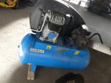a blue air compressor sitting on the ground next to a car