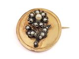 a gold brooch with pearls on it on a white surface