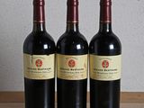trois bouteilles de vin rouge posées sur une table en bois, à côté d'une bouteille de vin