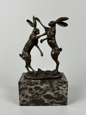 une statue en bronze représentant deux lapins qui se battent, posée sur un socle en marbre