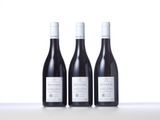 three bottles of red wine sit on a white table