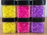 quatre bocaux remplis de perles de différentes couleurs posés sur une table en bois