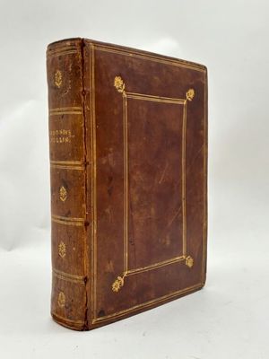 un vieux livre marron avec des bordures dorées posé sur une surface blanche