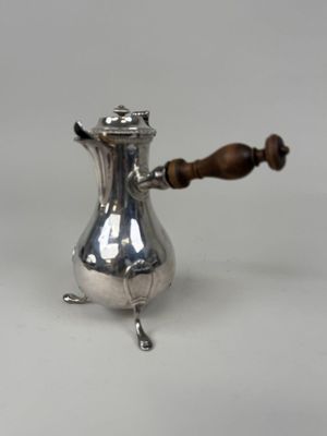 une cafetière ancienne en argent avec une poignée en bois, posée sur une surface blanche