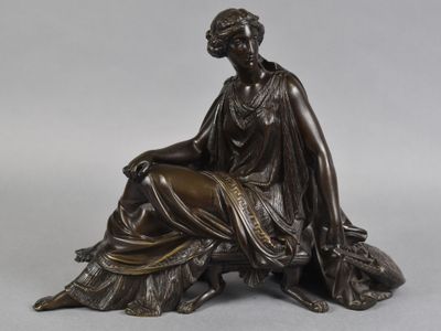 une statue antique en bronze représentant une femme assise sur un rocher