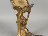 une statue en or représentant une femme tenant un miroir posé sur un socle