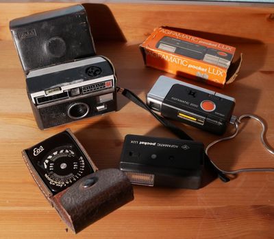 Plusieurs vieux appareils photo sont posés sur une table en bois, à côté d'autres objets