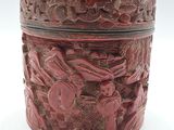 une boîte rouge ornée de sculptures, posée sur une surface blanche