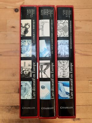 trois livres dans un étui rouge posé sur une table en bois
