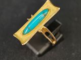 une image représentant une bague en or sertie d'une pierre turquoise sur un fond noir