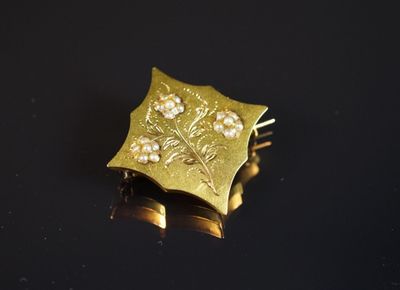 broche plaquée or jaune, ornée de fleurs et de perles sur un fond noir