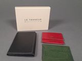 three different colored leather wallets sitting next to a white box