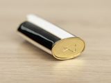 a close up of a gold and black lipstick on a wooden surface