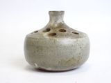 a small gray vase with holes in it on a white surface