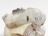 a white sculpture of a fish on a wooden stand