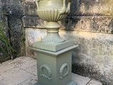 un grand vase vert posé sur un socle sur le trottoir