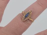 a woman ' s hand holding a gold ring with a blue stone