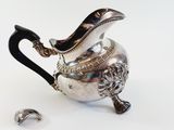 a silver teapot with a black handle and a silver spoon