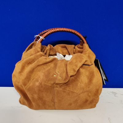 Sac à main marron à poignées tressées posé sur une table blanche devant un mur bleu