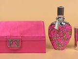 une boîte rose contenant un flacon de parfum et un verre à shot posés sur une table