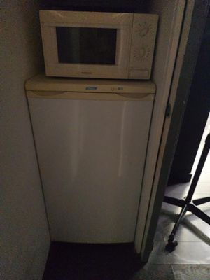 a small white refrigerator and a microwave in a small room