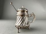 an antique silver teapot with a chain handle on a table