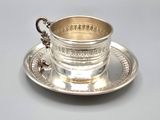 a silver cup and saucer sitting on a saucer