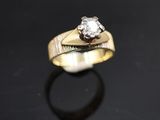 une bague en or sertie d'un diamant, posée sur un fond noir