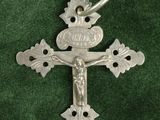 une croix en argent sur un tissu vert, avec un petit oiseau sur la croix