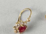 pair of gold and ruby earrings and a gold ring on a white surface