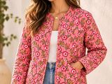 a woman wearing a pink jacket and jeans standing in front of a white wall