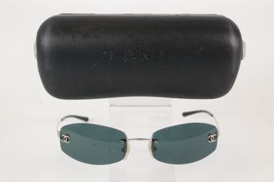 Lunettes de soleil Chanel et leur étui posés sur une surface blanche, avec un étui en cuir noir