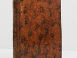 an old book with a brown cover sitting on a white surface