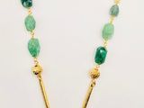 a gold necklace with green beads and a long chain