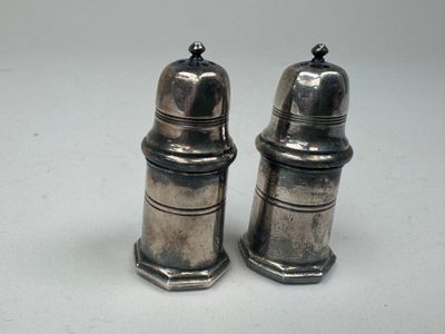 une paire de salières et poivrières en argent posées sur une surface blanche