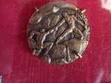 a silver medal on a red cloth with a picture of a man and a woman