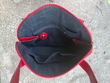 Quelqu'un tient un sac à main rouge et noir sur un trottoir.