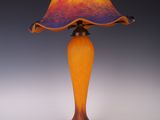 une lampe en verre orange et violet, avec un cordon noir, posée sur une surface blanche