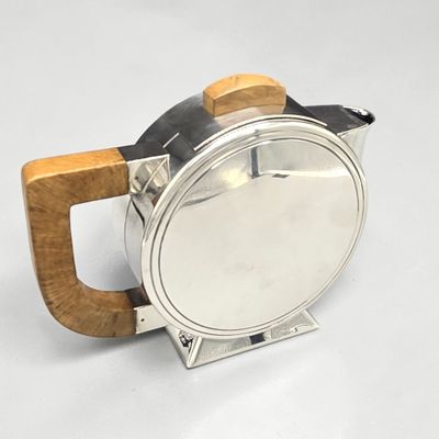 une théière en argent avec une poignée en bois posée sur une surface blanche