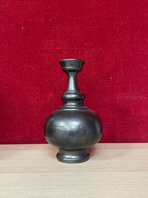 un vase noir posé sur une table, avec un mur rouge en arrière-plan