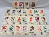 De nombreux timbres différents sont disposés sur une table recouverte d'une nappe blanche.