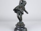 une statue en bronze représentant un garçon tenant un sac, posée sur un socle