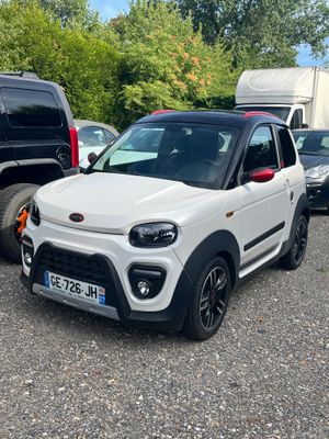 La petite voiture blanche est garée sur le parking, à côté d'autres voitures.