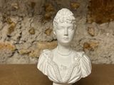 white bust of a woman on a pedestal with a stone wall in the background