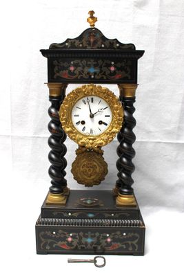 une horloge noire et dorée posée sur un socle, avec une clé
