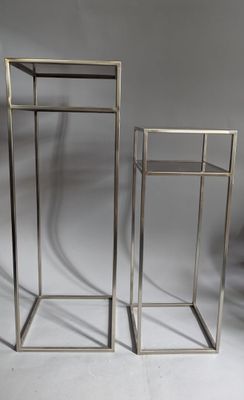 two metal stands with a glass top on a white surface