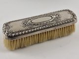 une brosse plaquée argent avec un manche, posée sur une surface blanche