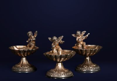 trois bougeoirs en argent ornés d'anges, sur fond bleu