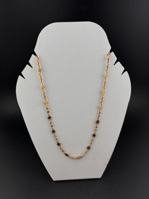 a gold chain necklace with black beads on a white mannequin